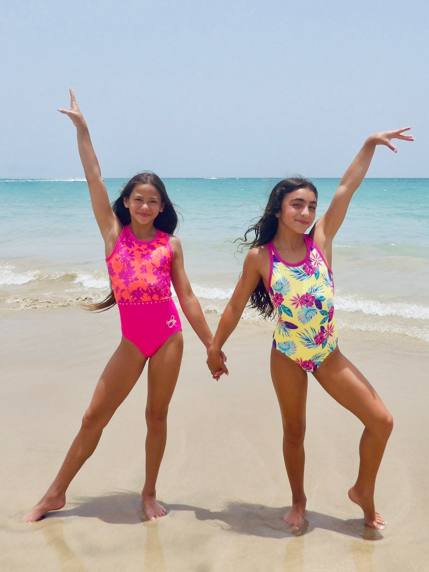 Two girls wearing Anaïs & Me leotards on a beach with ocean in the background