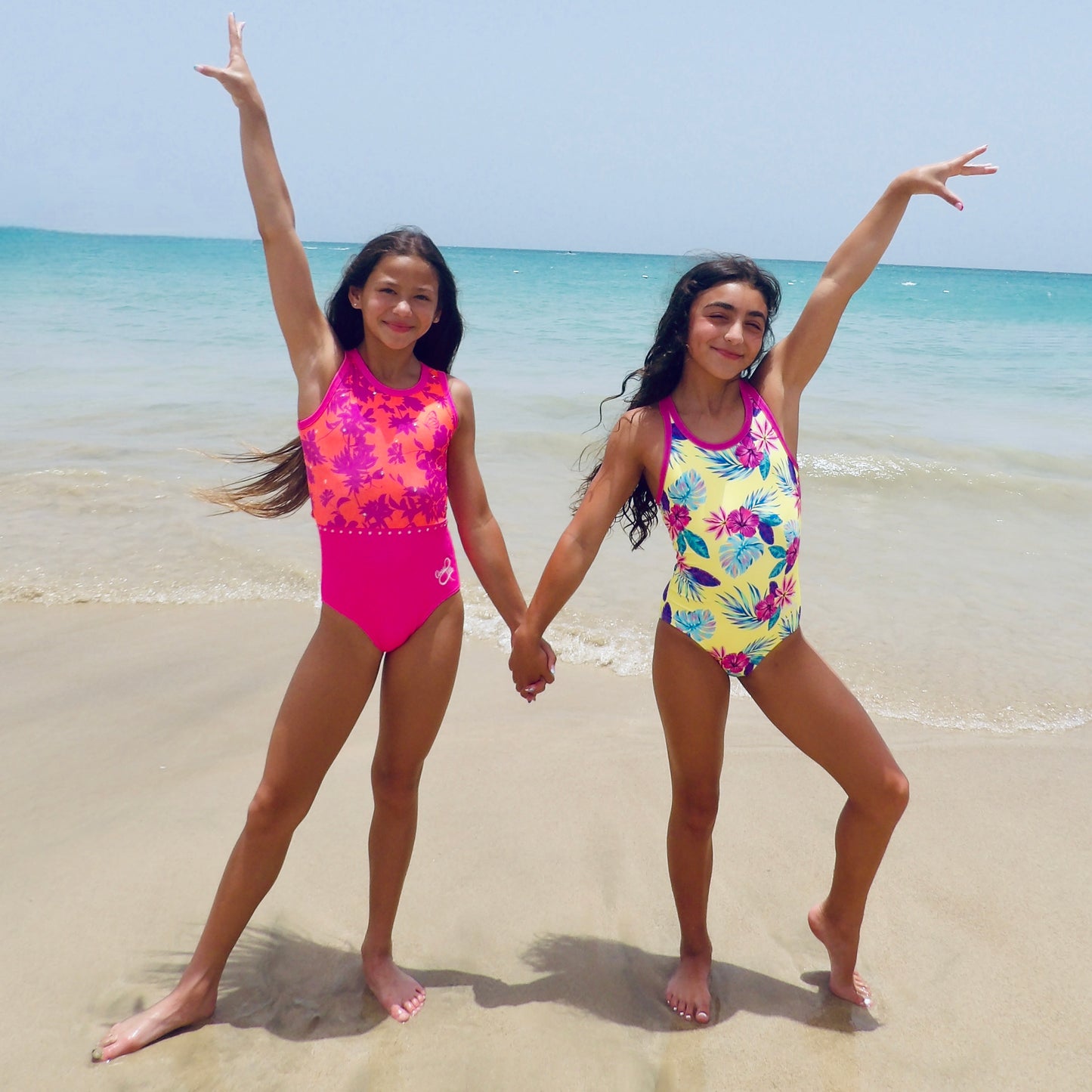 Two girls in colorful leotards on a beach with ocean in the background