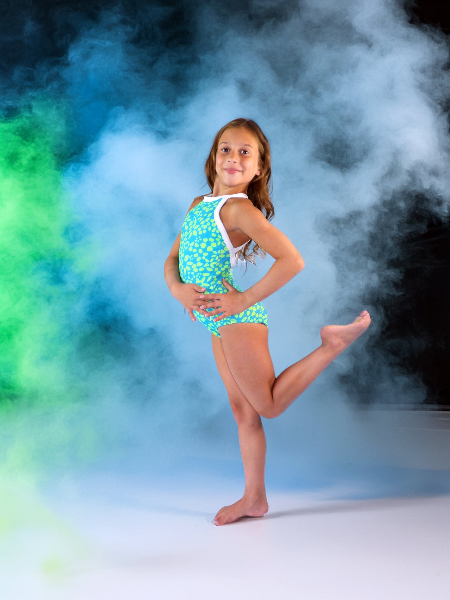 Young girl in a green and blue (Electric Floral) leotard posing in front of colorful smoke effects