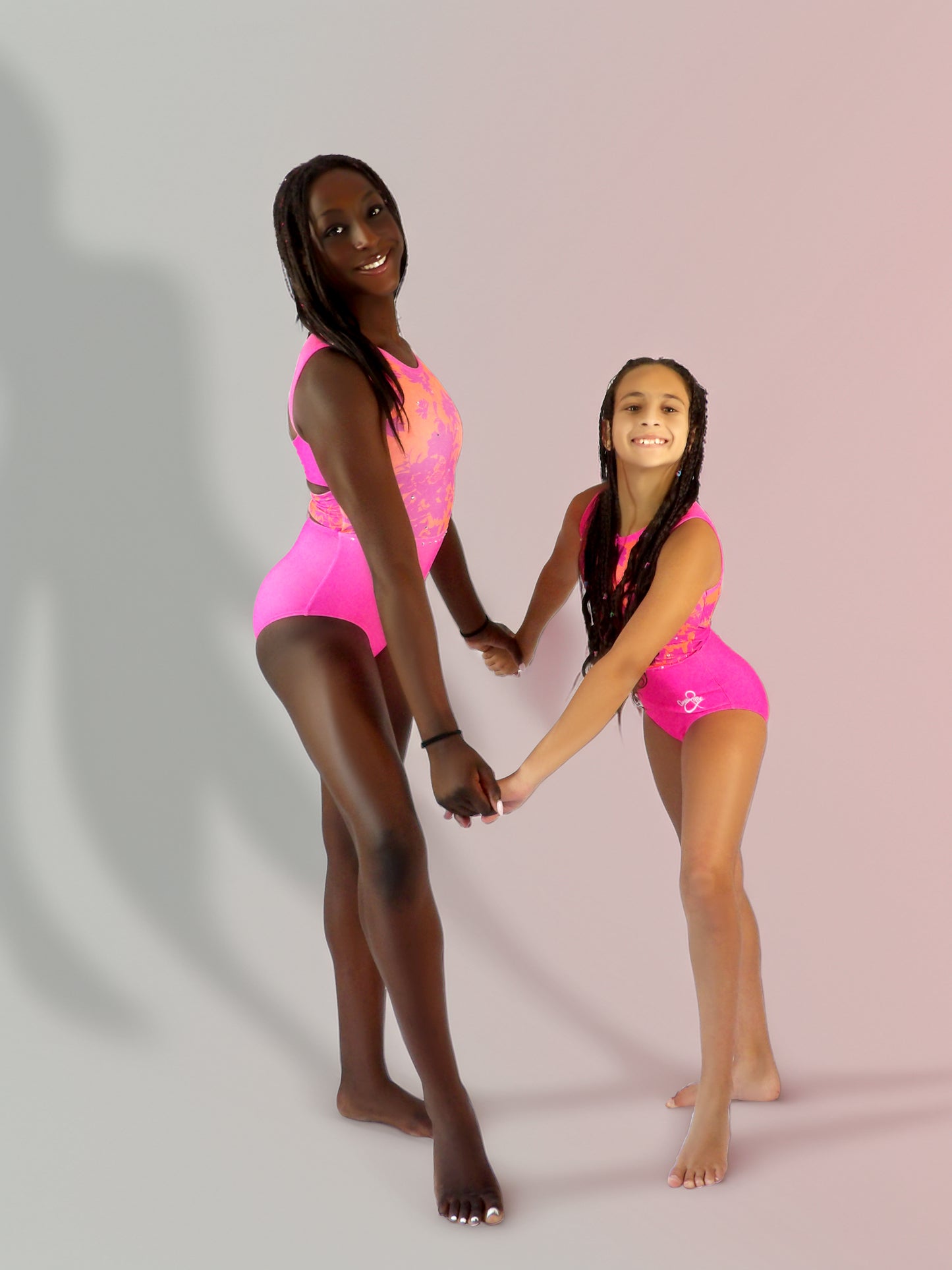 Two gymnasts wearing matching Mariposas leotards, celebrating friendship and confidence- neon pink and orange