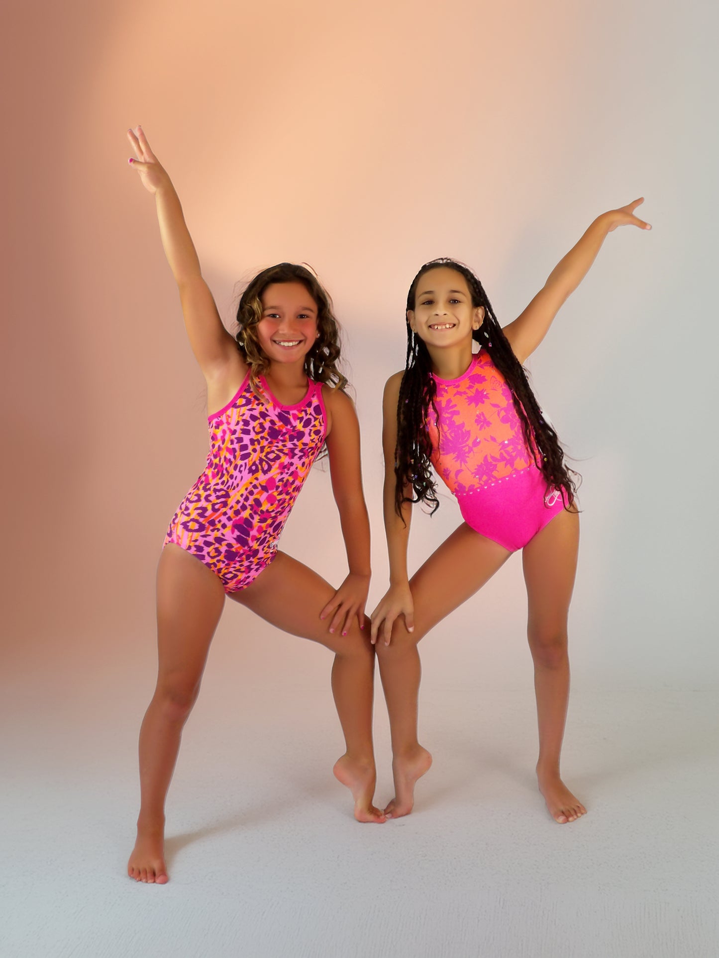 Two young girls in Mariposas & Safari Sorbet leotard posing against a gradient background