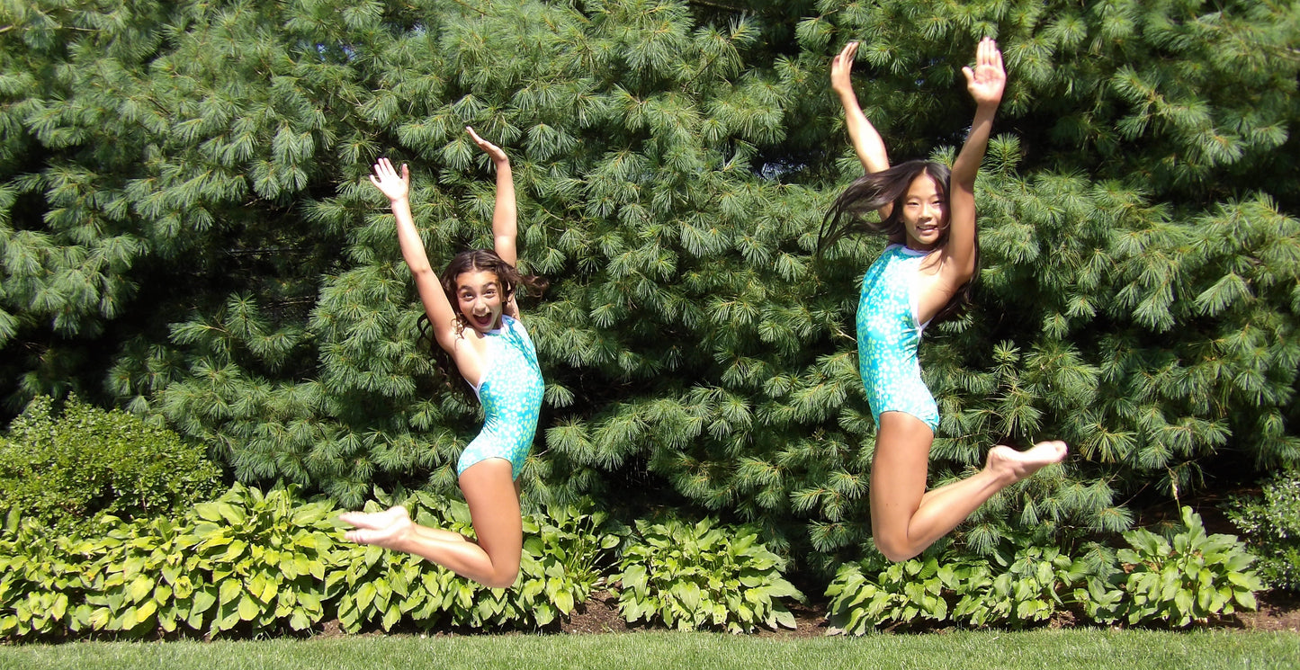 Two young girls in matching outfits jumping in the air against a green bush background